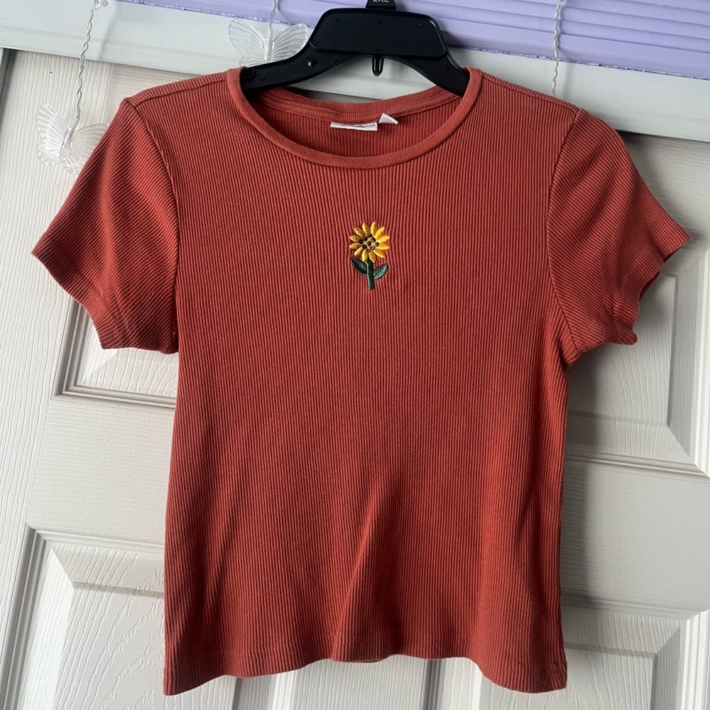 Tightly fitted and slightly cropped, reddish orangish color with sewn in flower.
